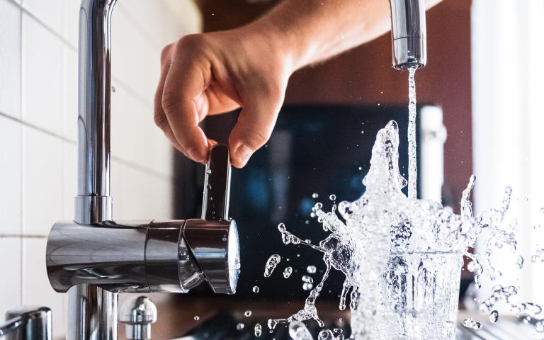 Arm som öppnar blandarkran och vatten rinner ner i ett dricksglas